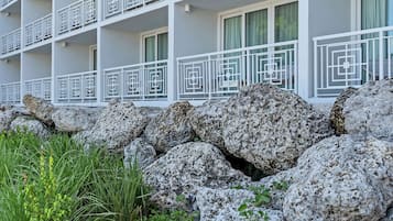 Un hotel de varios pisos con balcones, un jardín rocoso y plantas verdes.