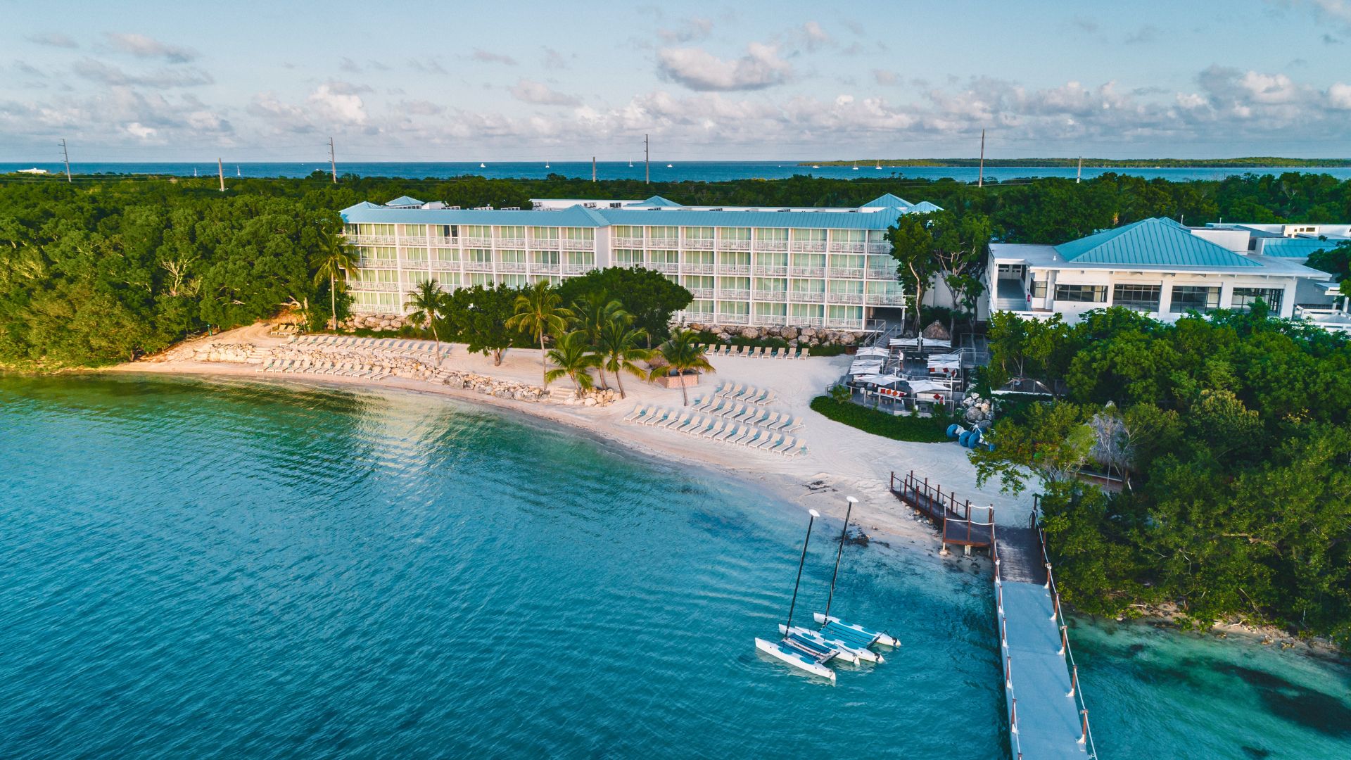 Un resort con playa, un muelle con barcos y un edificio grande con varios balcones.