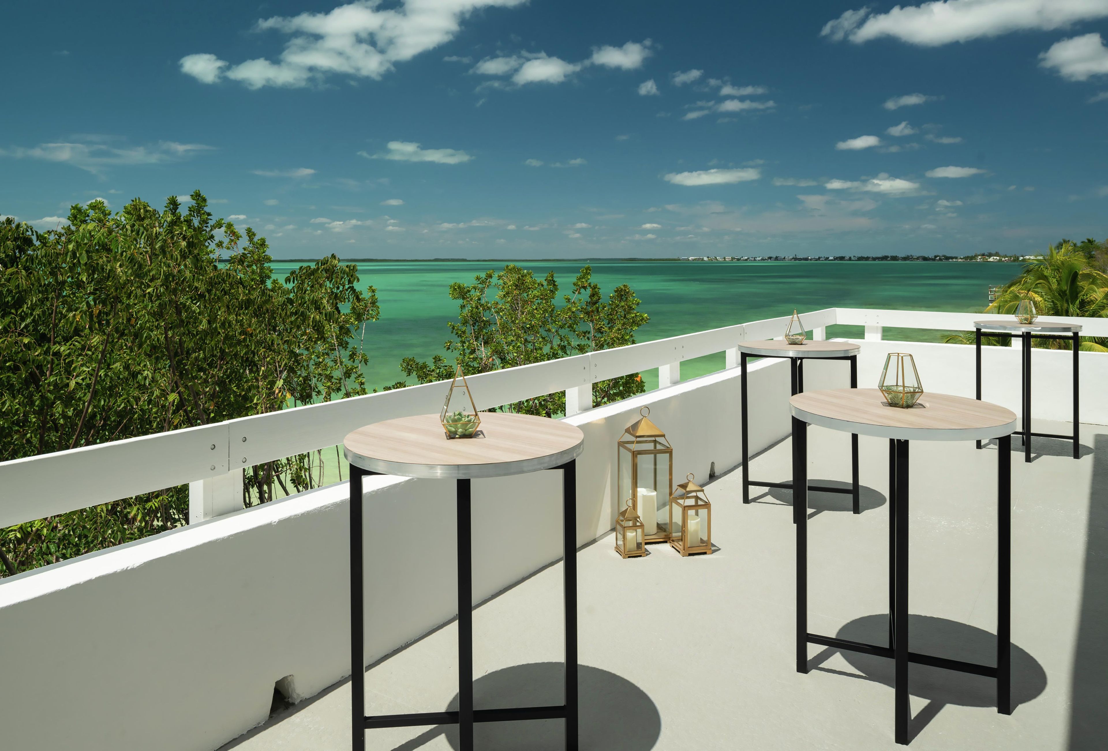 A balcony with round tables, a white railing, and a view of the ocean.