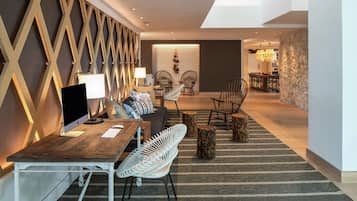 Un salon moderne avec un bureau en bois, un ordinateur et un canapé. Il y a deux fauteuils et une lampe. Le mur est décoré d’un motif et la pièce offre une vue sur une autre pièce où se trouve une table à manger.