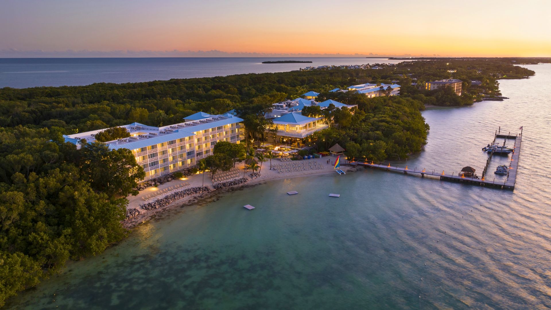 A resort with multiple buildings, a dock, and clear waters.