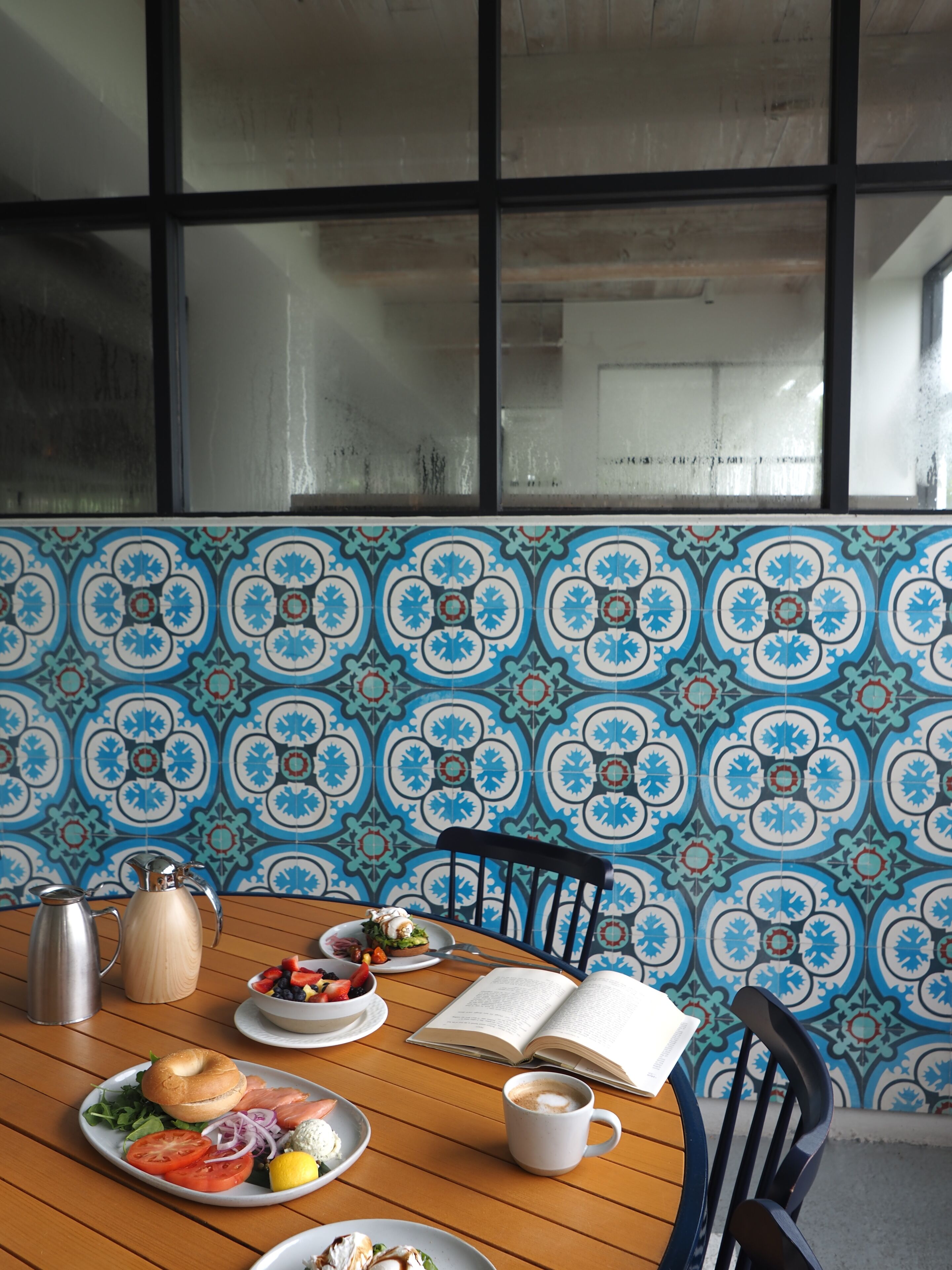 A dining table with plates of food, a coffee cup, and an open book.