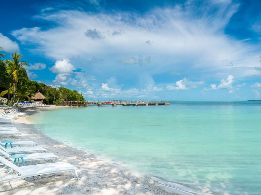 Une plage avec des chaises longues et une jetée qui s’avance dans l’eau.