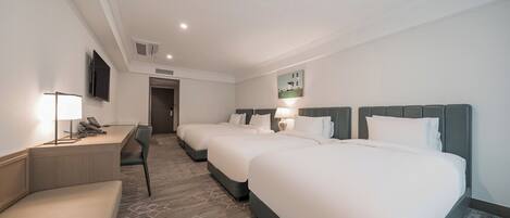 Habitación de hotel con tres camas, un escritorio con teléfono, una silla y un televisor en la pared.