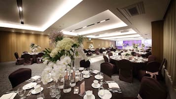 A banquet hall with round tables set for dining, each with white tablecloths, silverware, and floral centerpieces.