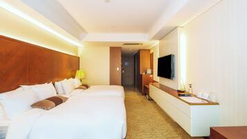Quarto de hotel com duas camas, televisão, escrivaninha e área de recepção.