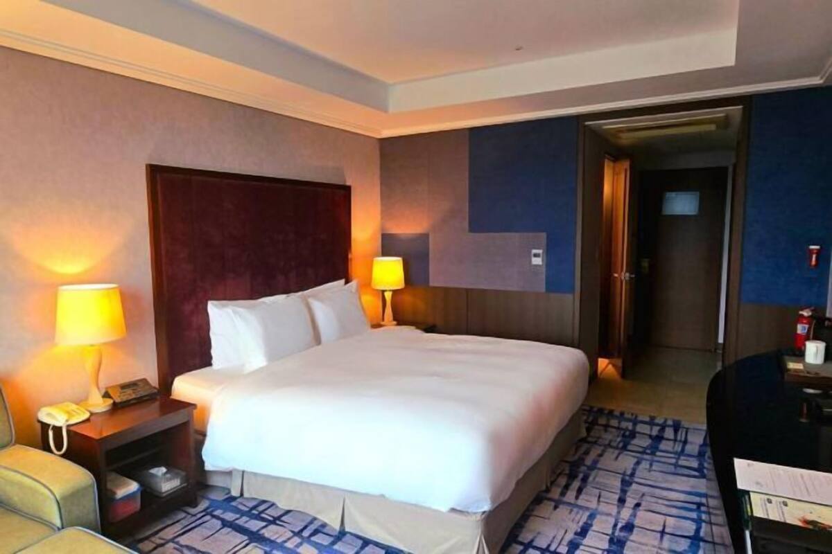 Ein Hotelzimmer mit einem großen Bett, zwei Nachttischlampen, einem Schreibtisch mit Lampe und einem Sessel.