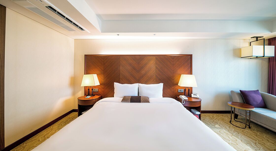 Une chambre d’hôtel avec un grand lit, deux tables de chevet avec des lampes, un canapé et une petite table.