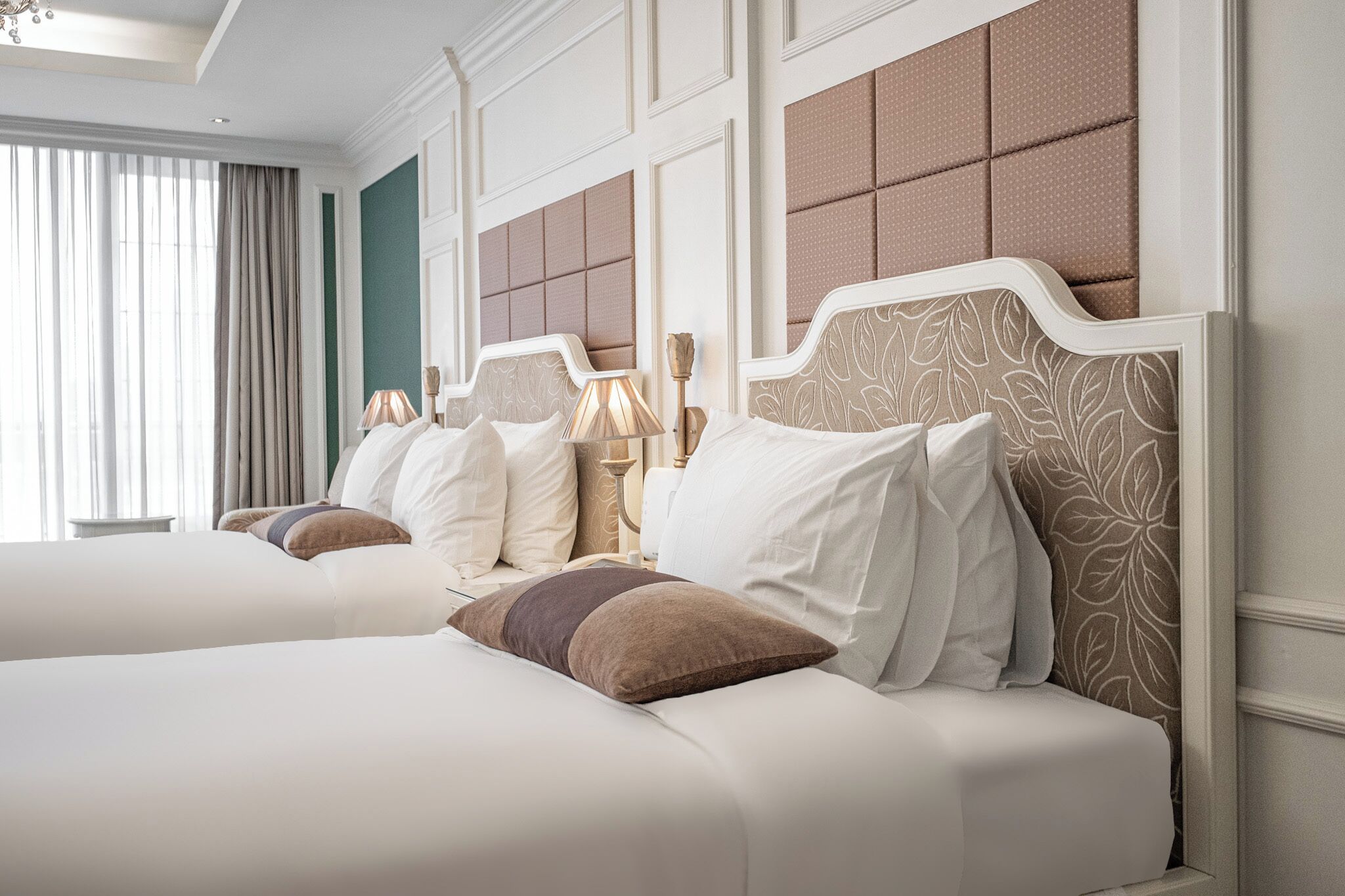 A hotel room with two beds, a large window with curtains, and a decorative headboard.