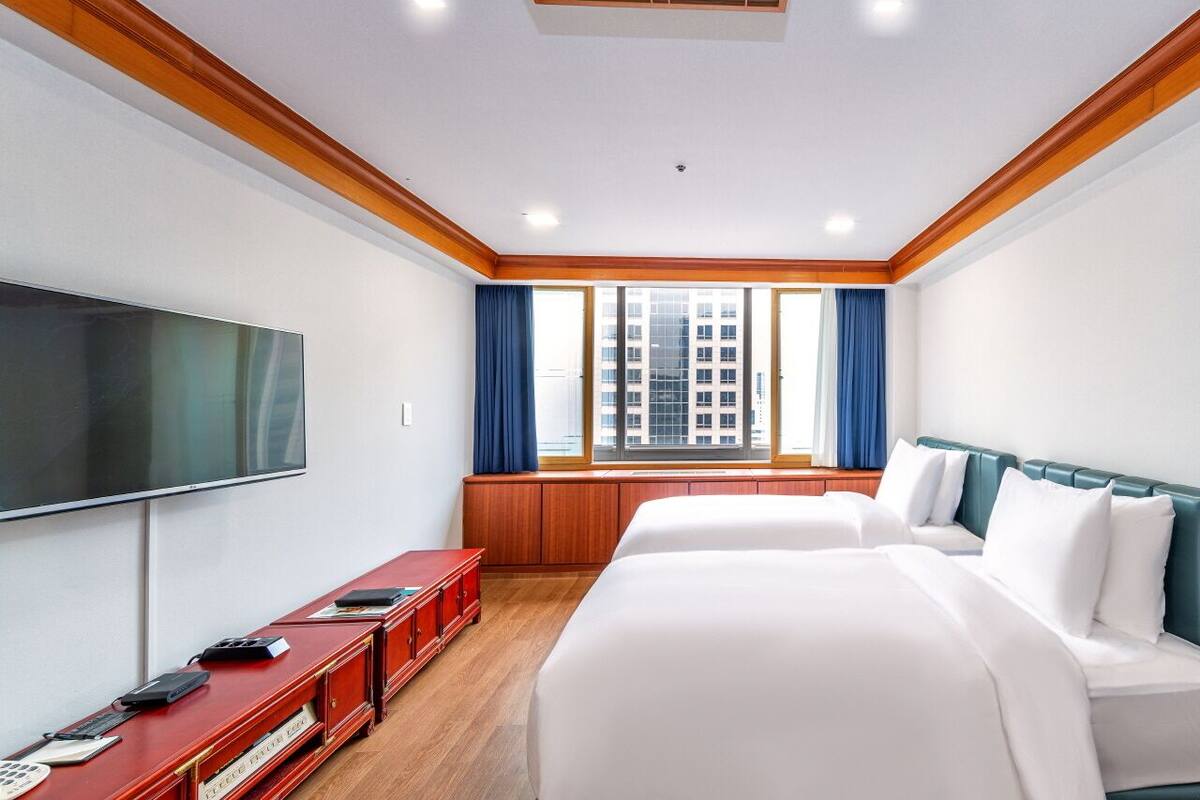 Ein Hotelzimmer mit einem großen Bett, einem Fernseher, einem roten Konsolentisch und einem Fenster mit Vorhängen.