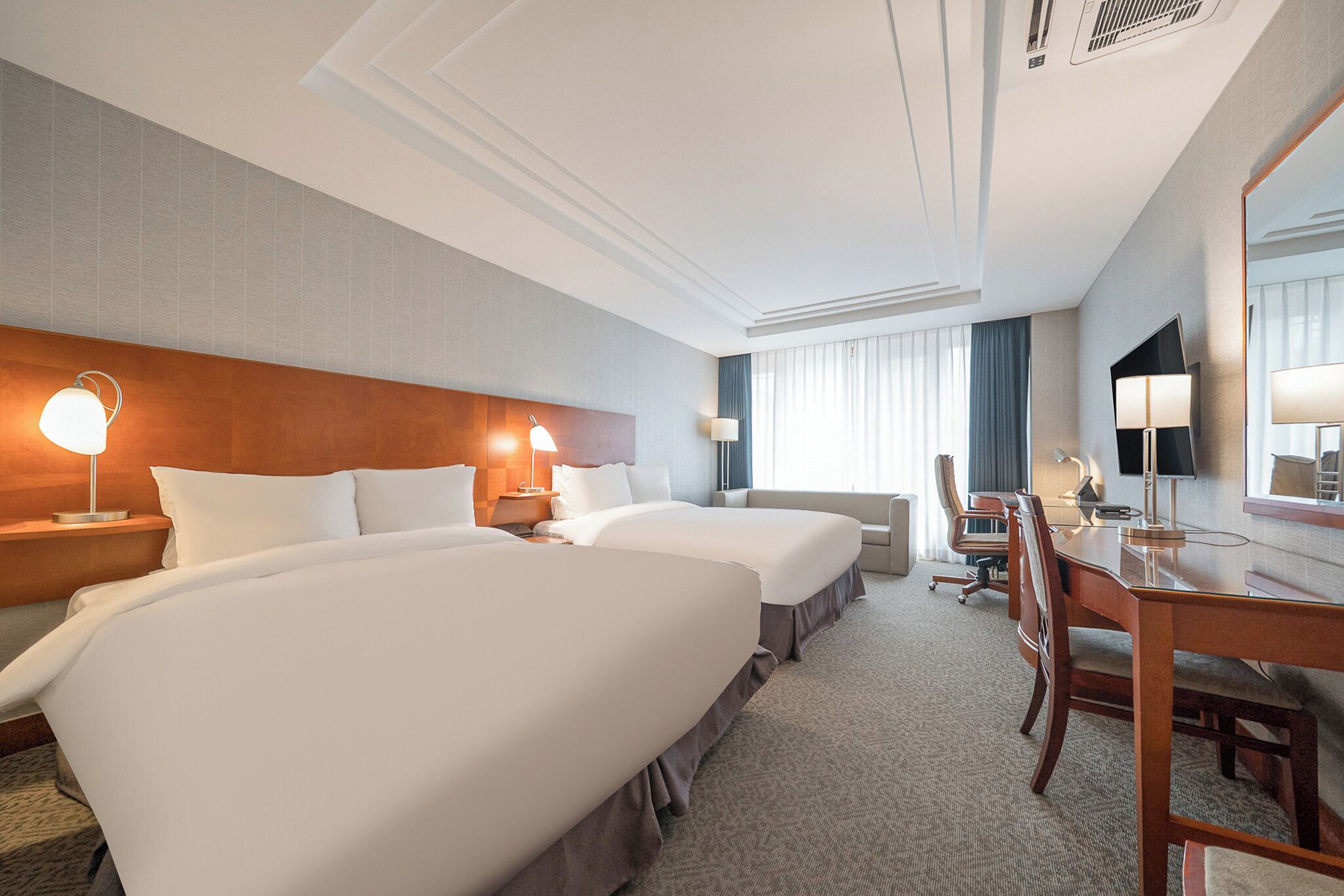 Habitación de hotel con dos camas, un escritorio, una silla, un televisor y un espejo grande.