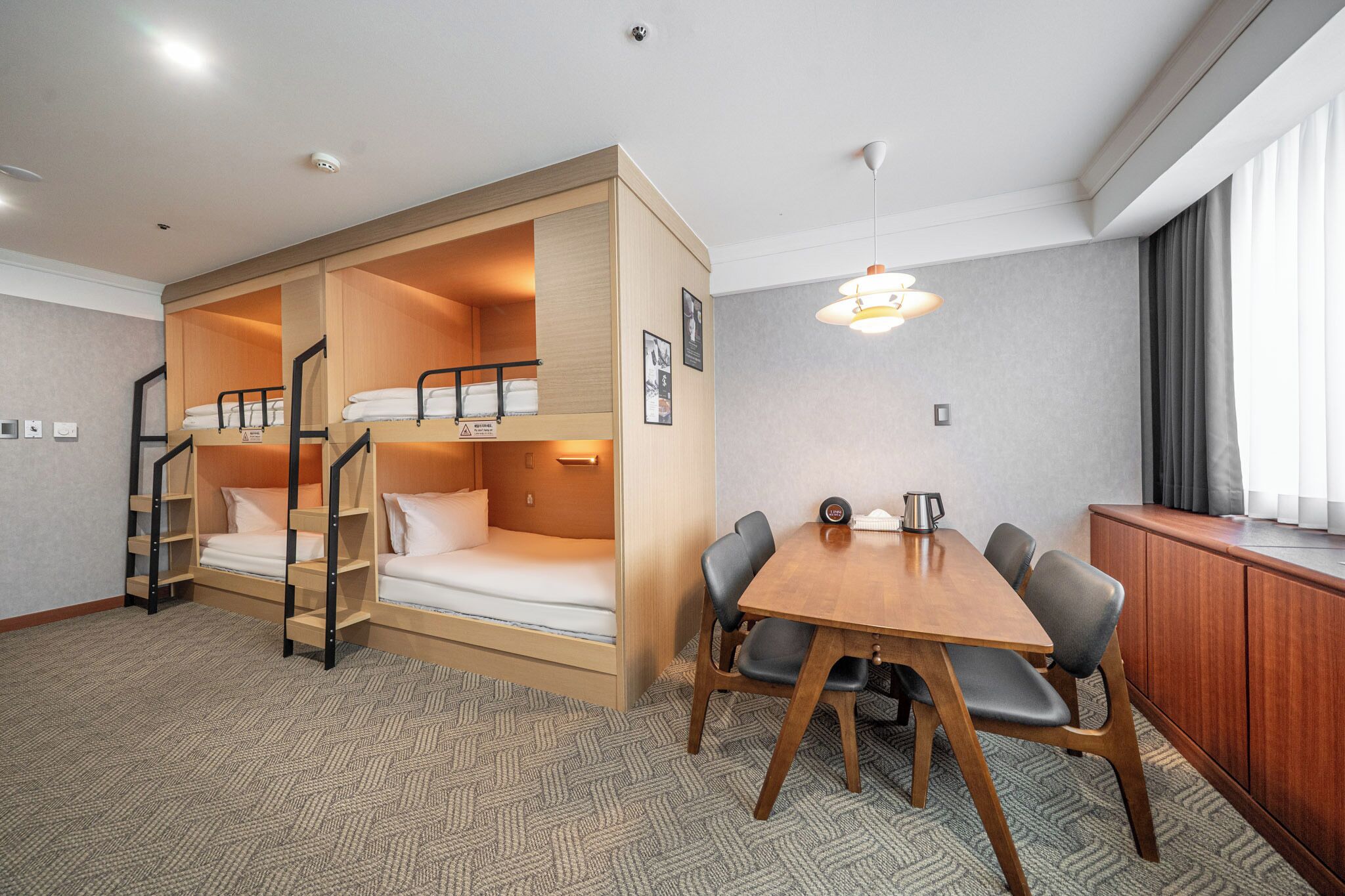 A room with bunk beds, a dining table with chairs, a cabinet, and a hanging light fixture.
