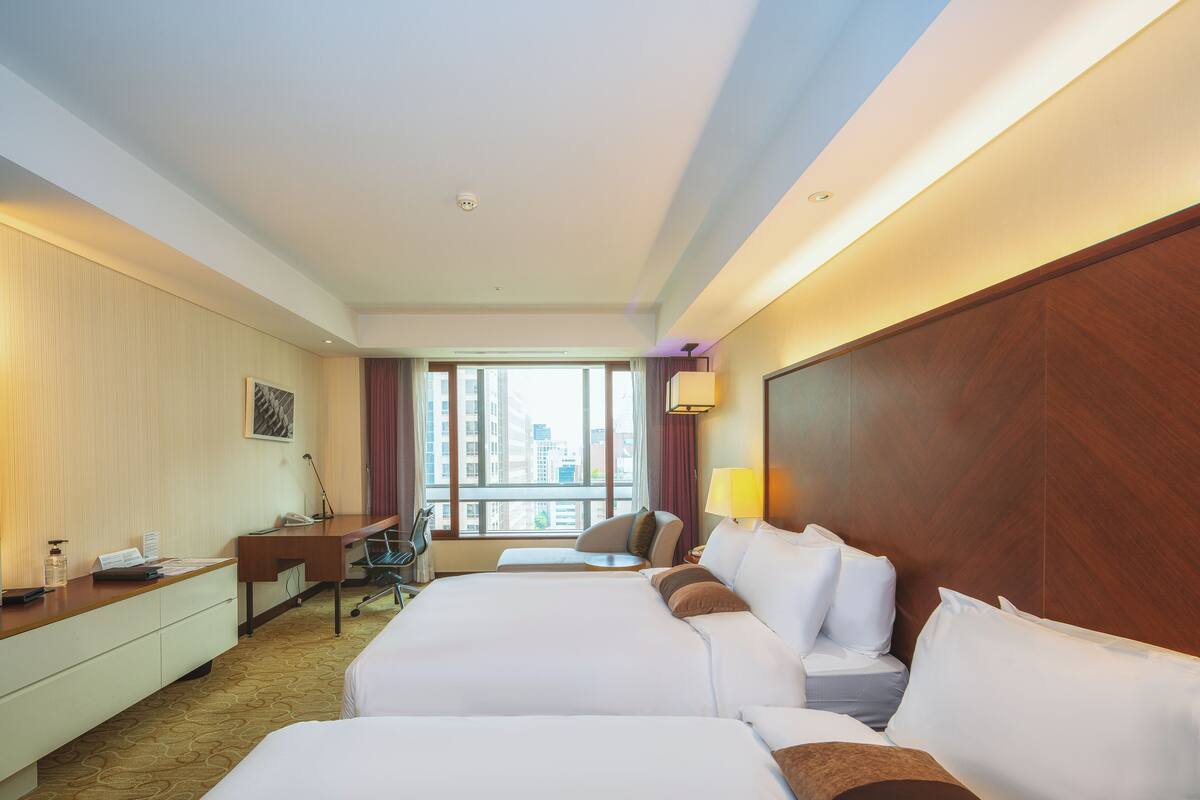 Ein Hotelzimmer mit einem großen Bett, einem Schreibtisch, einem Stuhl und einem Fenster mit Blick auf die Stadt.
