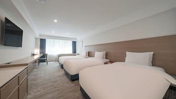 A hotel room with three beds, a desk, and a television.