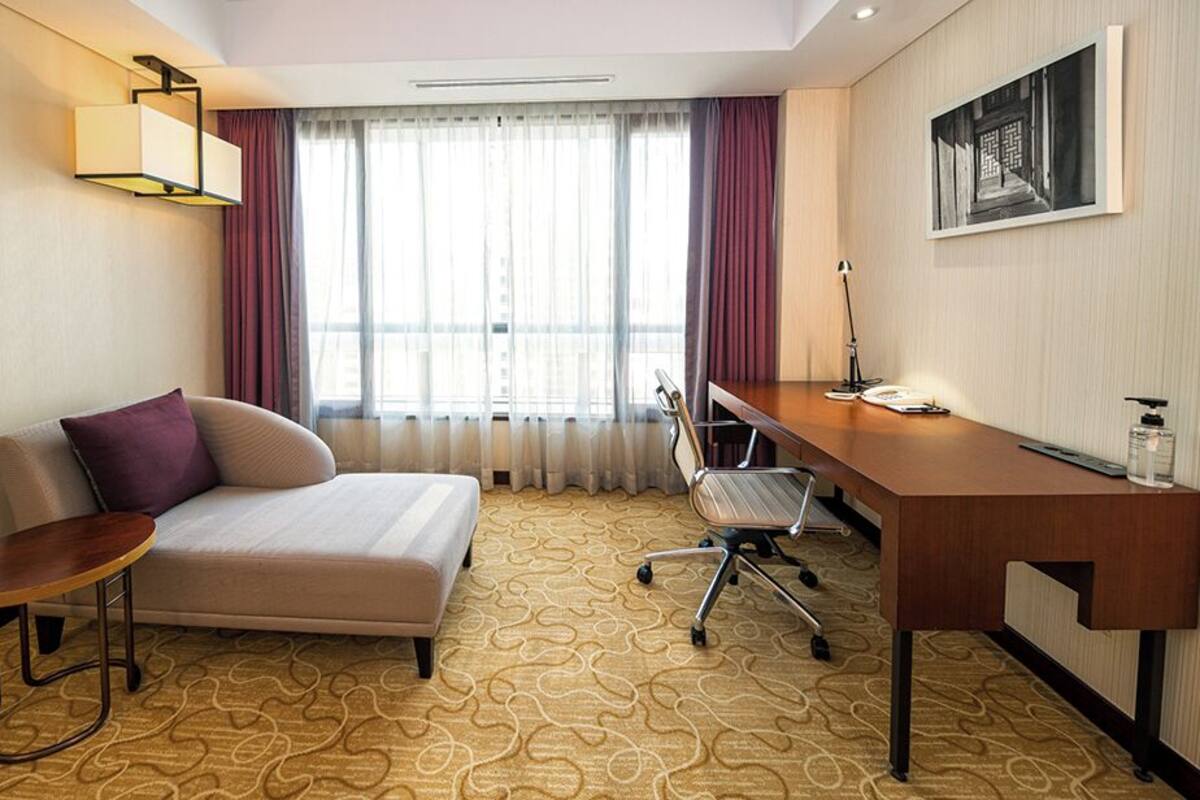 Ein Hotelzimmer mit Bett, Schreibtisch, Stuhl, kleinem Tisch und einem Fenster mit Vorhängen.
