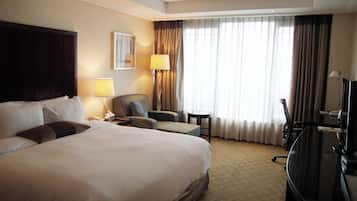 Habitación de hotel con una cama grande, un escritorio, una silla, un televisor y una ventana con cortinas.