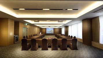 Un salón de conferencias con una larga mesa, sillas, una pantalla de proyector y piso alfombrado.