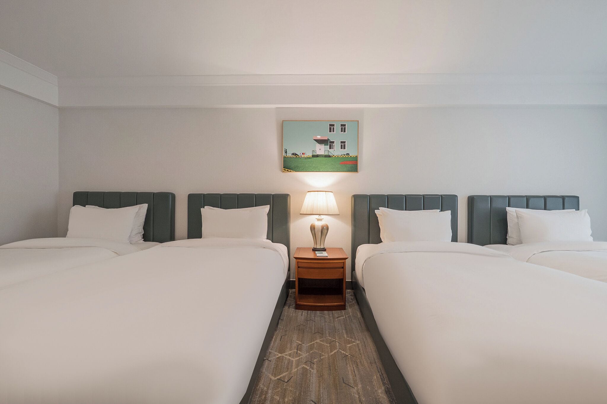 A hotel room with two beds, a nightstand with a lamp, and a painting on the wall.