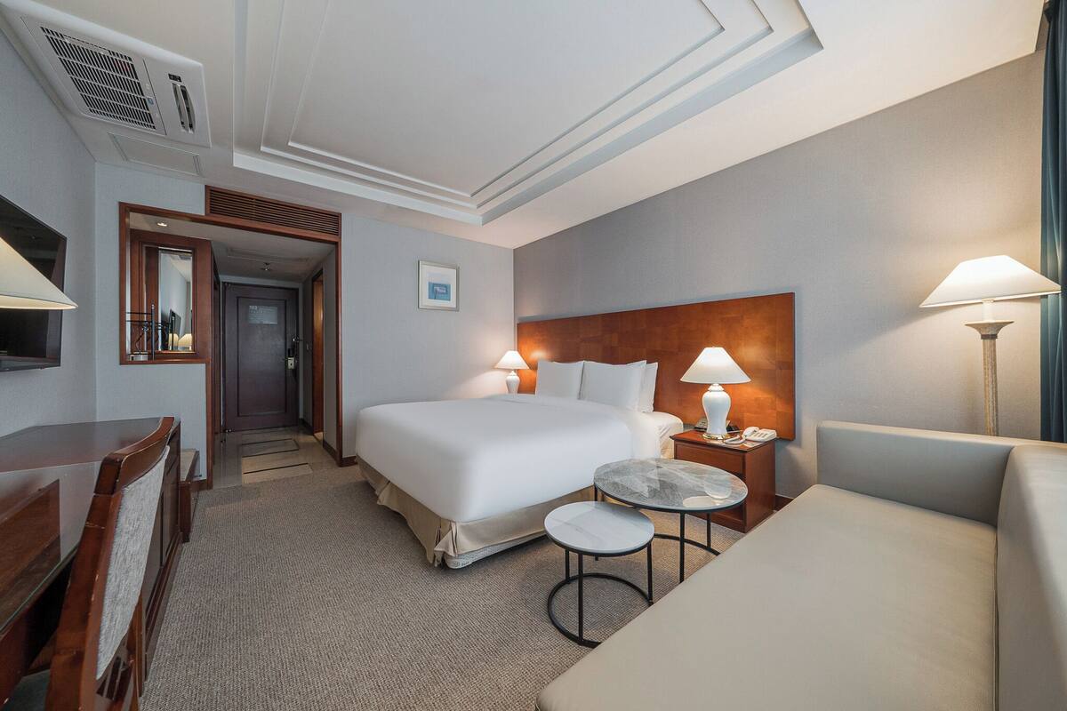 Ein Hotelzimmer mit einem großen Bett, Nachttischen, einem Schreibtisch, einem Stuhl und einem kleinen runden Tisch.