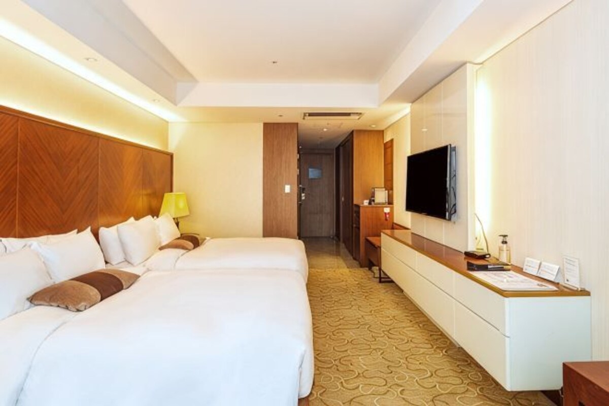A hotel room with two beds, a desk, a TV, and a reception area.