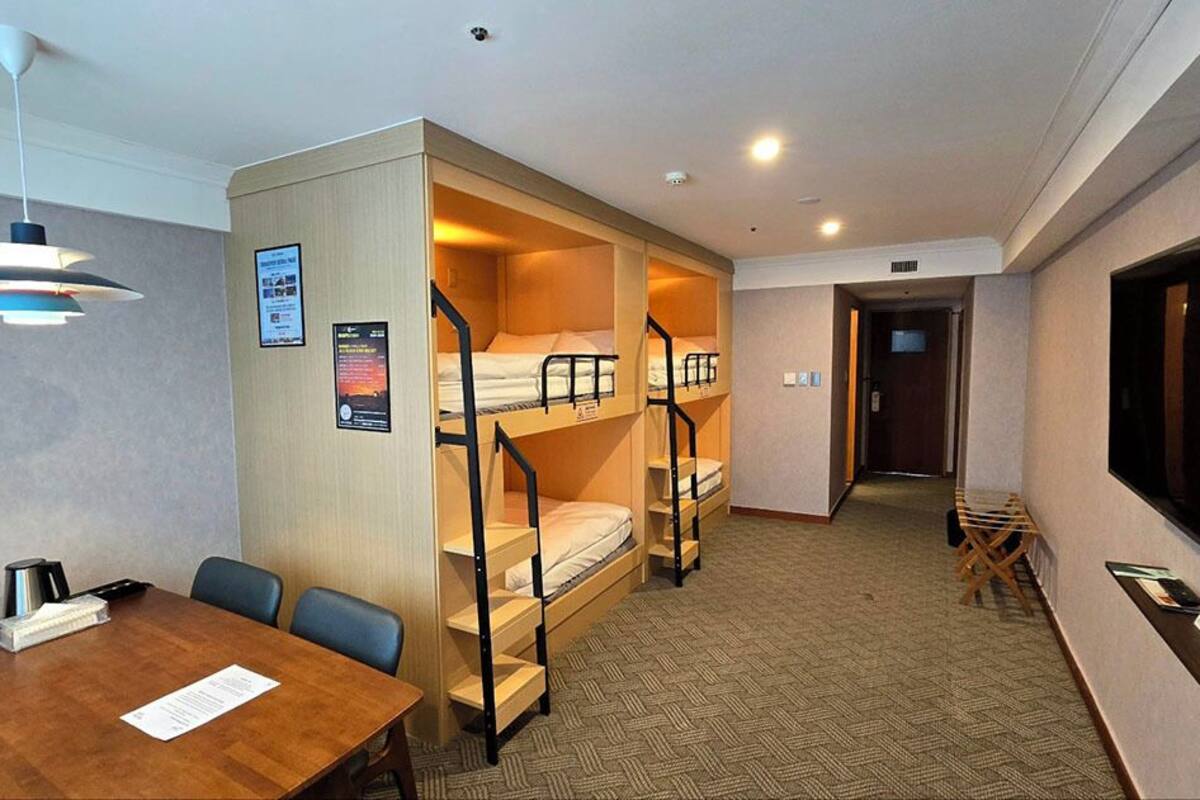 Ein Hotelzimmer mit Stockbetten, einem Esstisch, einem Fernseher und einem Schreibtisch.