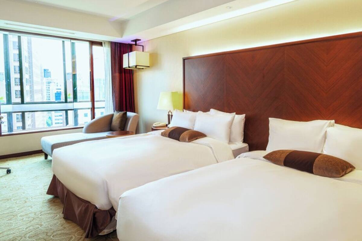Ein Hotelzimmer mit zwei grossen Betten, Blick auf die Stadt, einem Holzkopfende und einer kleinen Sitzecke.