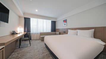A hotel room with a large bed, a desk with a chair, a television, and a window with curtains.