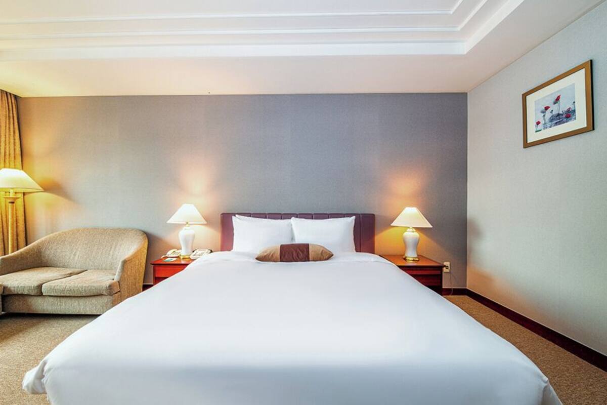 Ein Hotelzimmer mit einem großen Bett, zwei Nachttischlampen, einem Sessel und einem Nachttisch.