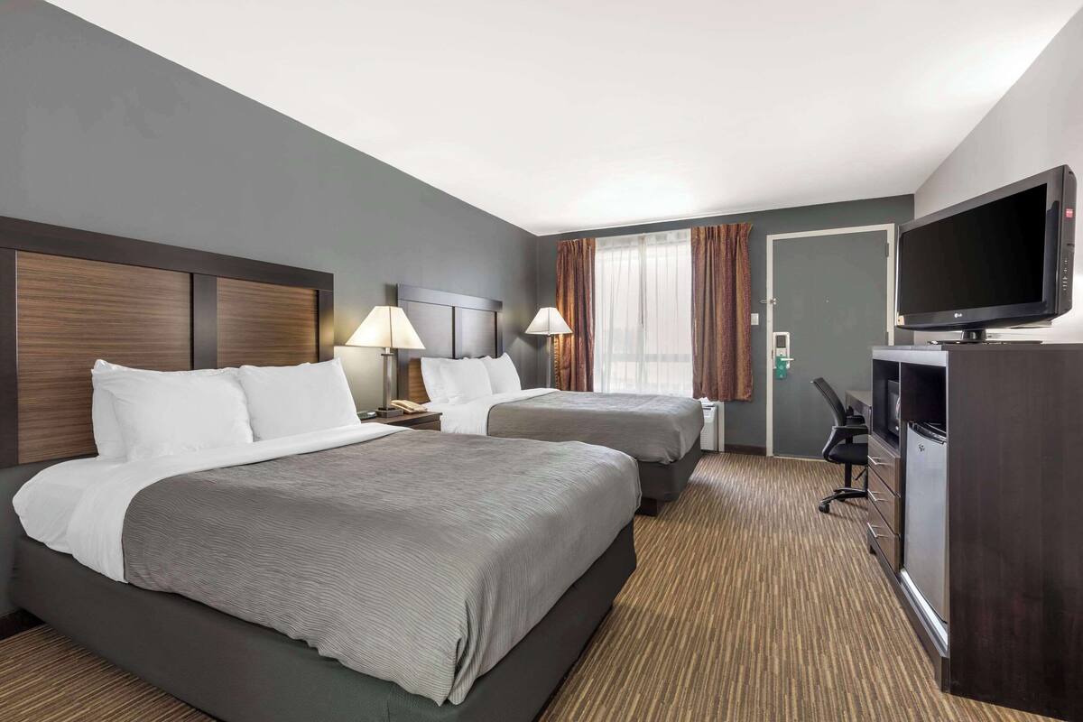 A hotel room with two beds, a television, a desk with a computer, and a minibar.