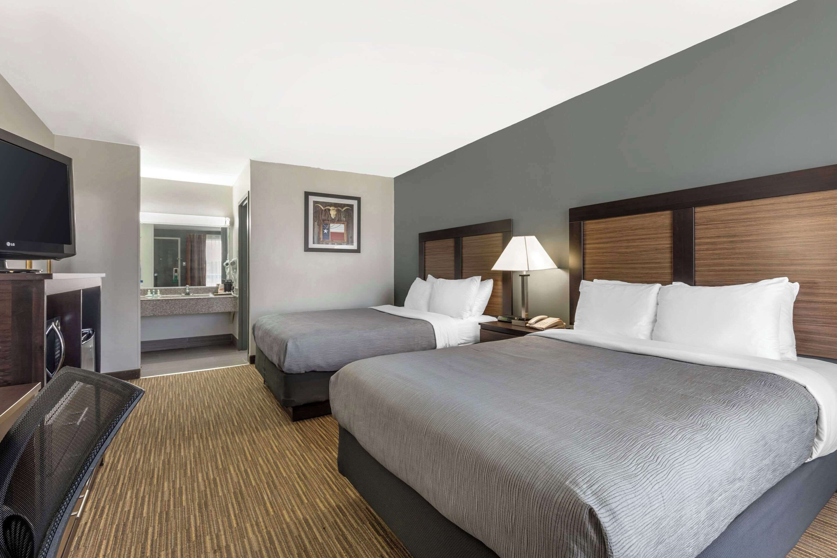 Habitación de hotel con dos camas, televisión, baño y escritorio con lámpara.