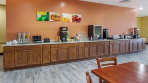 A breakfast bar with coffee machines, a refrigerator, and a seating area with a wooden table and chairs.
