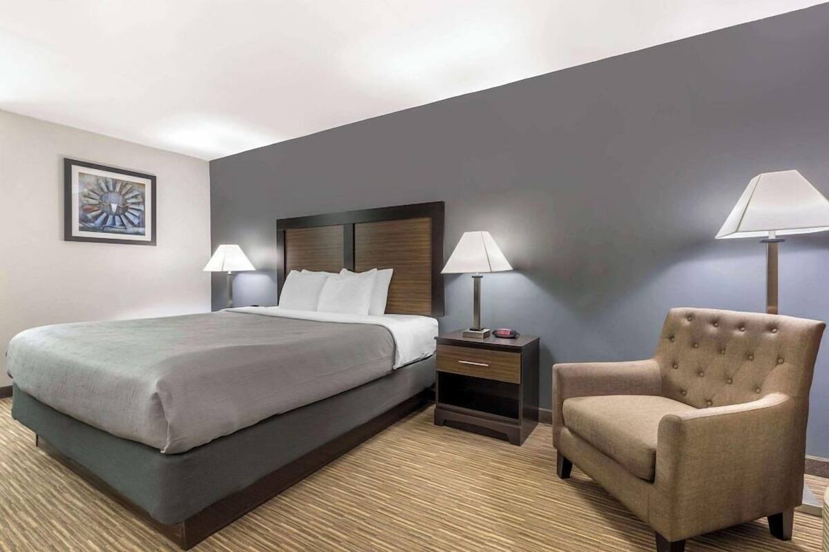 A hotel room with a large bed, two bedside tables with lamps, a chair, and a framed picture on the wall.