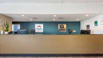Un mostrador de recepción de hotel con una pared verde azulado, dos letreros que dicen "Suburban Studios by Choice Hotels" y "Quality by Choice Hotels", y una computadora sobre el mostrador.