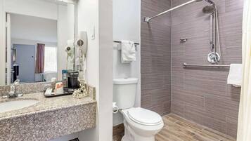 A bathroom with a granite countertop, a white toilet, a shower with a handheld showerhead, and a towel rack.