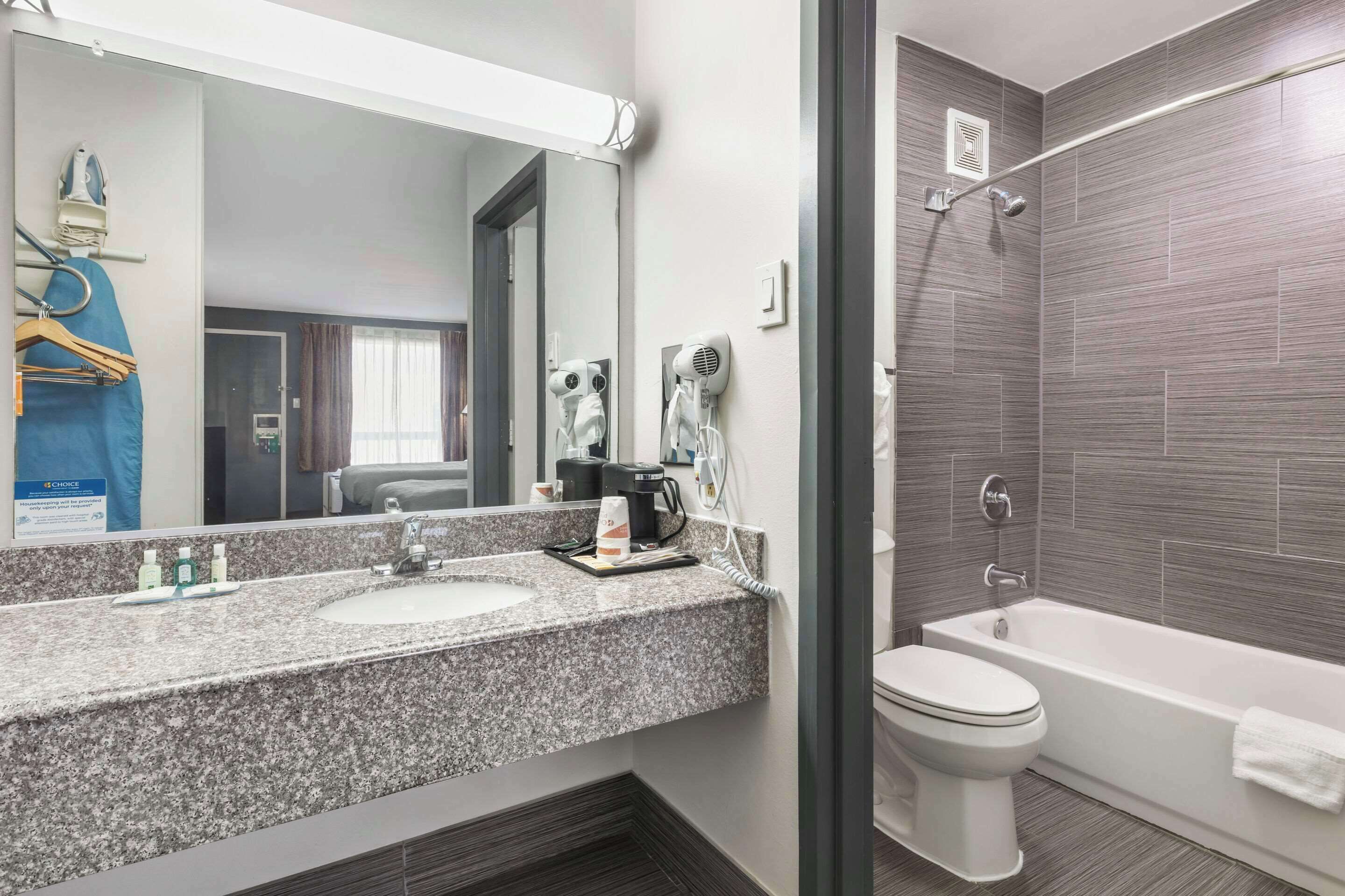 A modern bathroom with a granite countertop, two sinks, a toilet, and a shower.