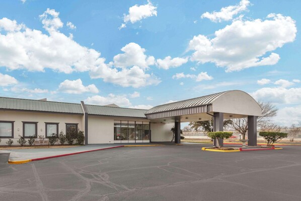 A building with a covered entrance, a parking lot, and a clear sky with clouds.