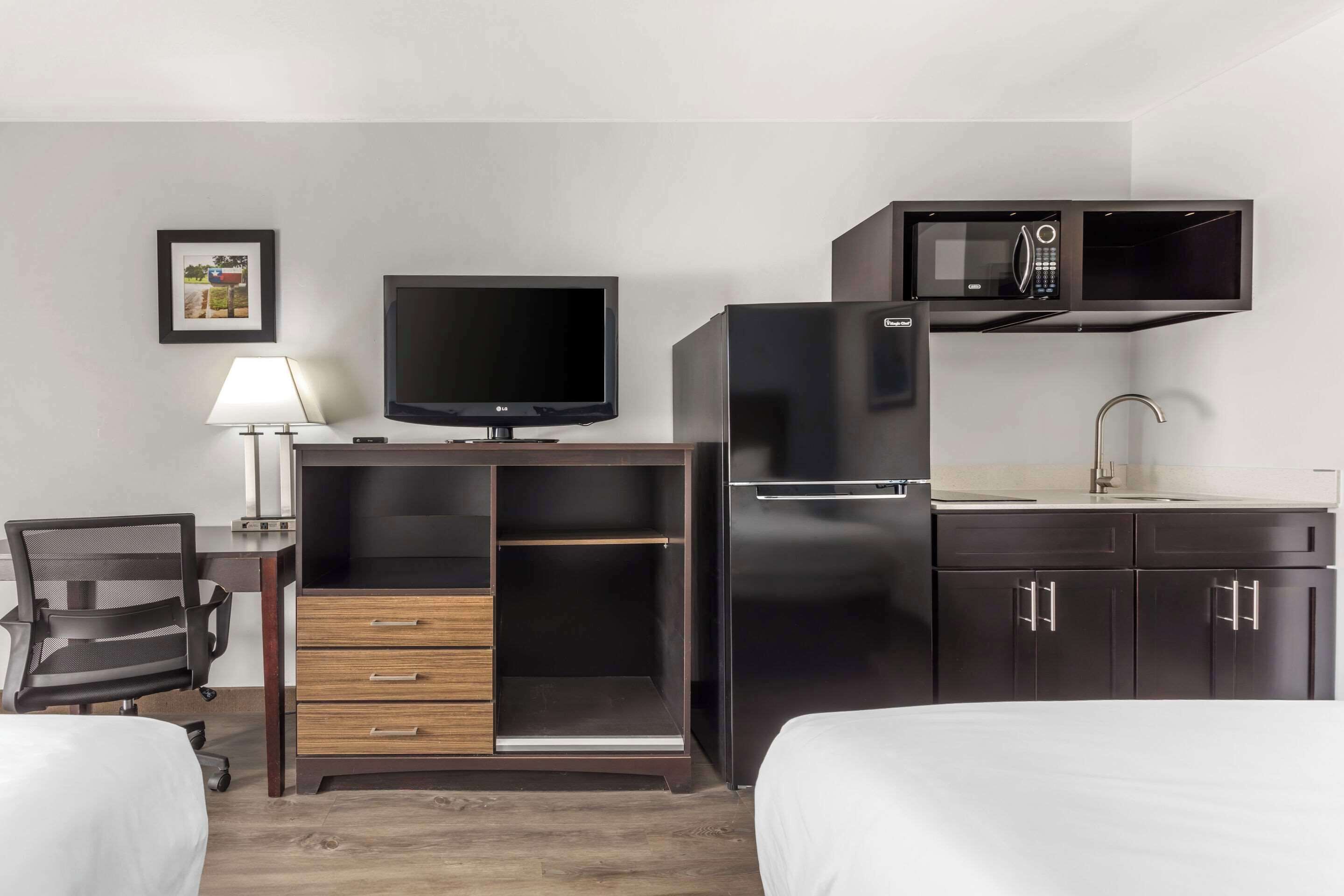 Habitación de hotel con cama, escritorio con computadora, televisor, microondas y refrigerador.