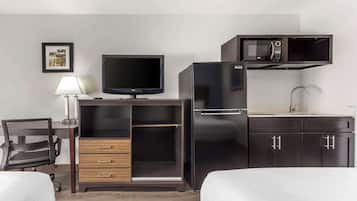Habitación de hotel con cama, escritorio con computadora, televisor, microondas y refrigerador.