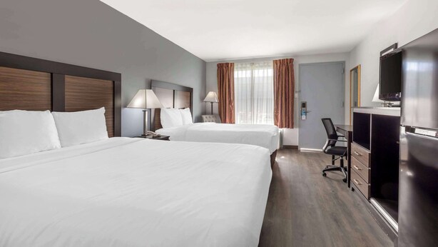 A hotel room with two beds, a desk with a chair, a television, and a minibar.