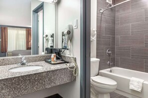 A modern bathroom with a granite countertop sink, a hairdryer, and a bathtub.