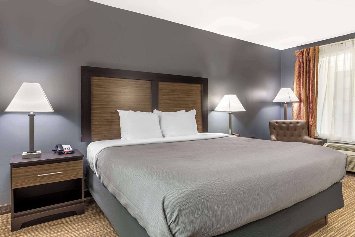 A hotel room with a large bed, two bedside tables with lamps, a chair, and a window with curtains.