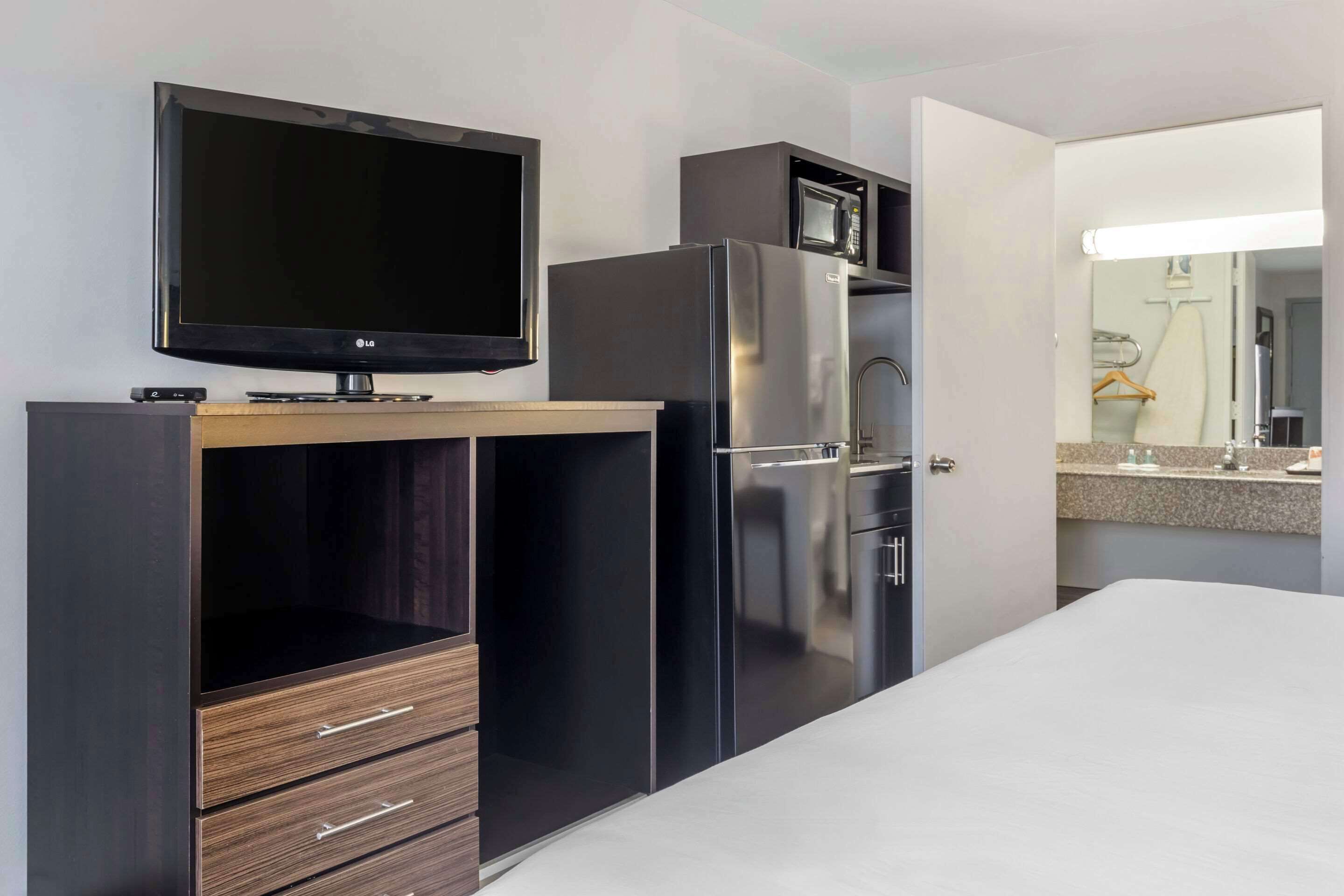 Ein modernes Hotelzimmer mit Flachbildfernseher, Kühlschrank, Mikrowelle, Holzschrank und einem Bett.