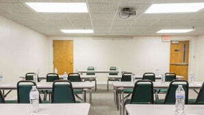 Un salón de conferencias con varias mesas, sillas, botellas de agua y un proyector.
