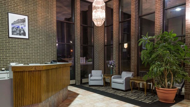 Un área de recepción con un mostrador de madera, dos sillones blancos, una mesita y una planta en maceta.