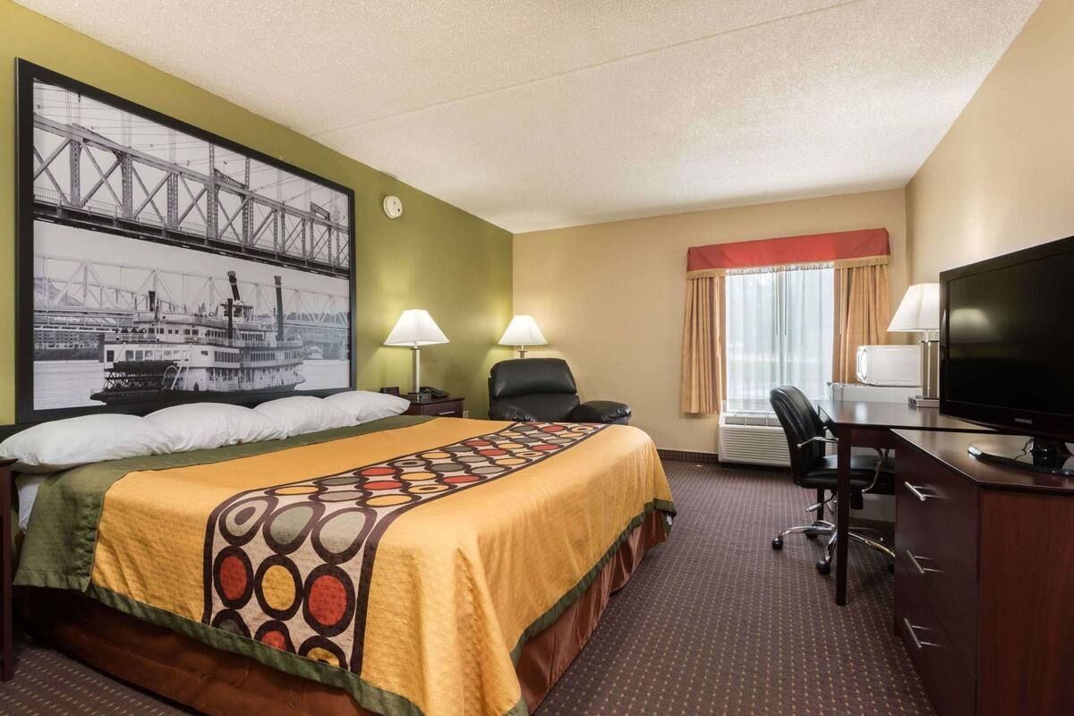 Ein Hotelzimmer mit Bett, Schreibtisch, Fernseher und einem großen, gerahmten Bild einer Brücke.