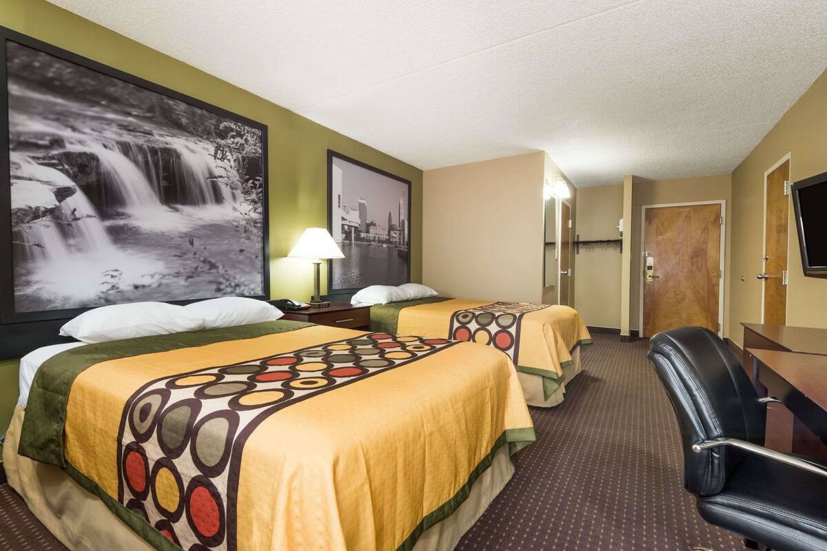 Ein Hotelzimmer mit zwei Betten, einem Schreibtisch, einem Stuhl, einem Fernseher und einem großen Wandbild mit einem Wasserfall.