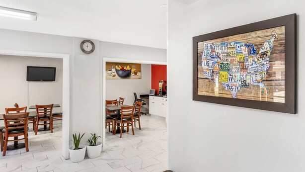 Un comedor con sillas de madera y una mesa, una cocina con pared roja y un reloj, y una obra de arte colgada en la pared que muestra el mapa de EE. UU.