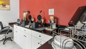 Una zona de cocina con máquinas para hacer gofres, una cafetera y un cartel que indica la hora del desayuno.