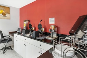 A kitchen area with waffle makers, a coffee machine, and a sign indicating breakfast time. - Econo Lodge Research Triangle Park (Durham)