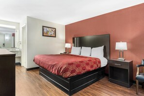 A hotel room with a bed, bedside tables, a chair, and a desk. - Econo Lodge Research Triangle Park (Durham)